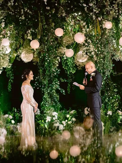 A couple shares their vows against an enchanted forest backdrop. This intimate moment is framed by a wall of lush greenery and soft, glowing orbs, creating a truly magical and romantic setting.