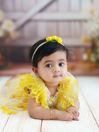 A lovely tummy-time photo from a milestone session. Lying on a rustic wood floor with a floral backdrop, this baby girl gives the camera a sweet, calm look.