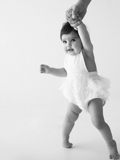 Those first wobbly steps while holding onto a helping hand are a milestone to cherish. This black and white image focuses on the motion and determination of a baby learning to walk.