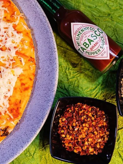 Create, inspire, innovate. A freshly made pizza served with classic condiments like chili flakes, oregano, and Tabasco sauce, ready to be customized.