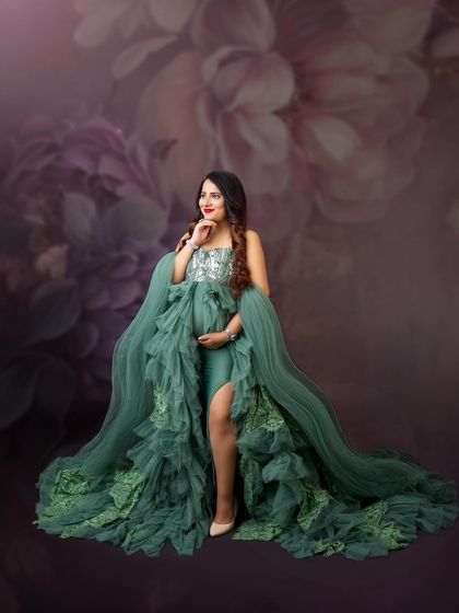 An elegant olive green gown with intricate lace details, set against a beautiful floral painted backdrop.