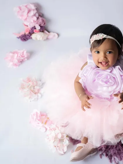 Celebrating her first birthday in style. This little princess is all smiles in her pink and lavender tutu, surrounded by flowers and a floral number '1' prop.