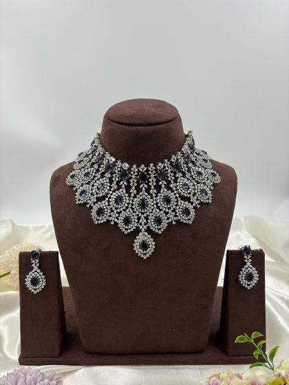 A heavy, silver-plated AD necklace set with a peacock-inspired feather design. This statement piece is available in blue, green, pink, and all-white.