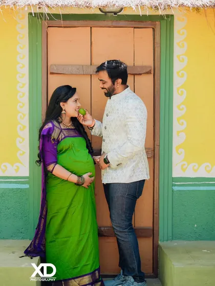 A playful and sweet moment during a traditional themed shoot, where the partner offers a raw mango to the mother-to-be.