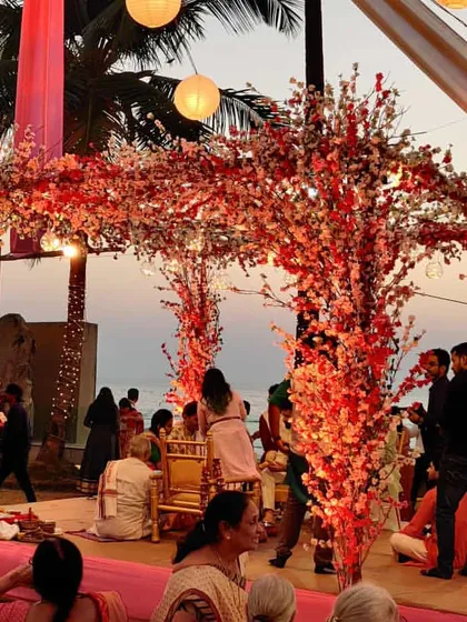 We love using unique elements like these cherry blossom trees to frame a mandap. The vibrant red and white flowers create a stunning contrast against the pink stage and the blue sea.