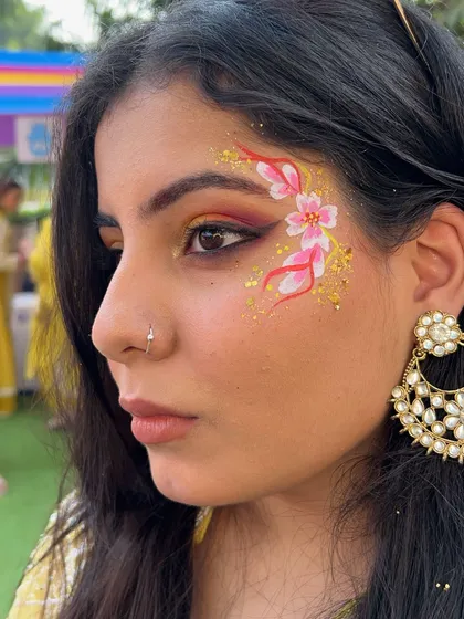 Floral designs are always in demand. This look combines delicate pink flowers with a sprinkle of gold glitter, perfect for a daytime event or a mehndi function. It's a beautiful example of how face art can complement a traditional look.