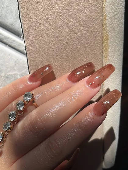 A beautiful, sun-kissed shot of these sheer brown jelly nails with delicate glitter. It's a subtle yet stunning look.