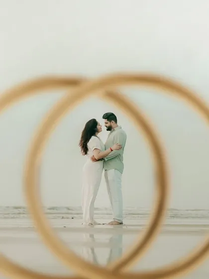 A creative shot framing the couple through their wedding rings. This unique pre-wedding photo symbolizes their union against the backdrop of the ocean.