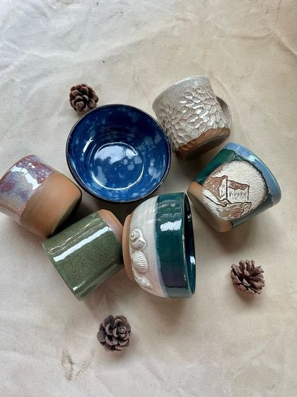 A collection of student-made mugs and bowls, showcasing a variety of textures and glaze combinations.