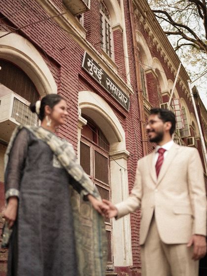 A classic shot in front of the historic "Mumbai Samachar" building. The warm tones and the couple holding hands create a sense of timeless romance, perfect for their vintage-themed pre-wedding shoot.