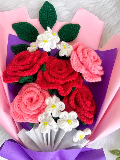 A close-up of the red and pink rose bouquet, highlighting the detailed crochet work on the roses and the delicate white accent flowers.