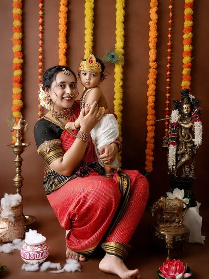 A mother holds her baby Krishna, who is wearing a peacock feather in his hair, creating a classic and adorable festive look.
