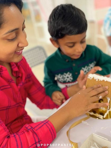 A mother guides her son's hand as they apply icing, working together to build their sweet holiday decoration.