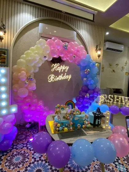 A pastel rainbow-themed birthday party, with a multi-colored balloon ring and a neon "Happy Birthday" sign.