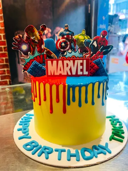 A powerful Marvel-themed cake with red and blue drips, featuring Iron Man, Captain America, Hulk, and Spiderman.