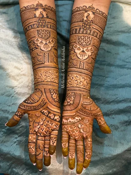 This bridal mehendi showcases symmetrical designs on both hands, featuring peacock motifs and detailed patterns that extend up the forearms. The artistry creates a balanced and harmonious look.