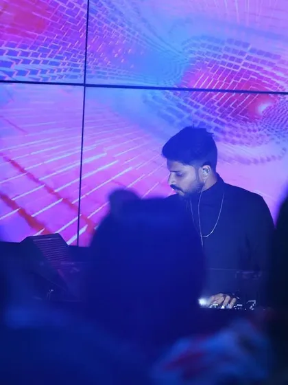 A shot from the crowd's perspective, showing me at the decks against a mesmerizing purple and blue visual display. The goal is to create a complete sensory environment where the music and visuals feel like one.