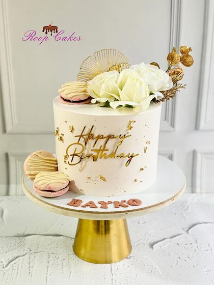Elegant birthday vibes for 'Bayko' (wife). This stunning white and gold cake is adorned with roses, macarons, and a personalized touch.
