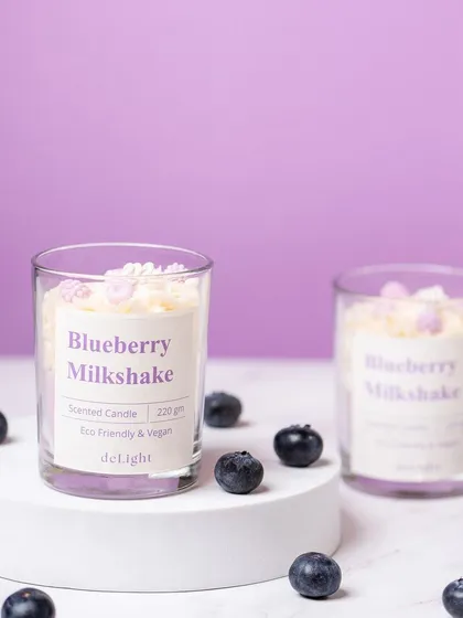 A minimalist shot of a Blueberry Milkshake scented candle, styled with fresh blueberries. The clean, purple-themed composition is modern and appealing.