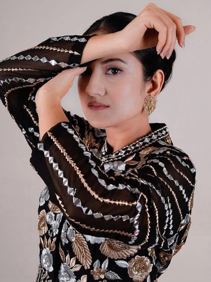 A creative headshot where the model's hands frame her face. This pose adds an artistic element while still showcasing the detailed craftsmanship of the blouse and the professional makeup artistry.