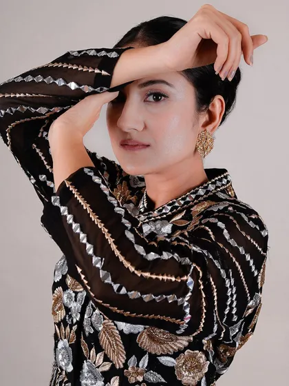 A striking beauty portrait where the model's hands frame her face, showcasing both her flawless makeup and the detailed sleeve of her outfit. This composition is both elegant and powerful.