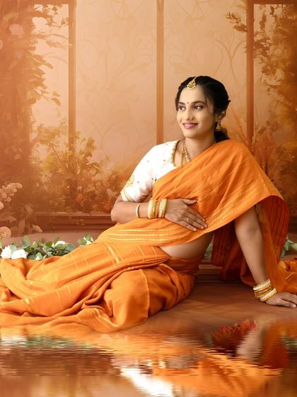A beautiful reflection shot of a mom-to-be in a golden-orange saree, seated by a digitally created water effect, adding a touch of magic.