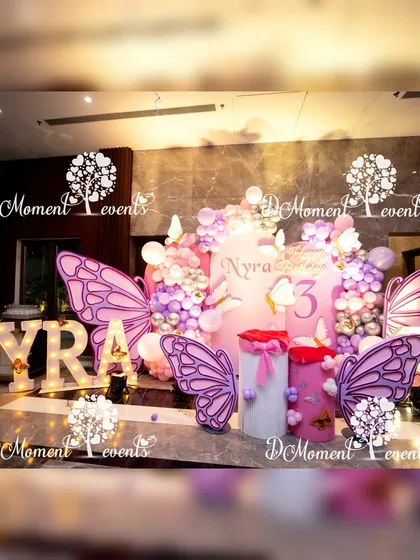 A magical stage for Nyra's 3rd birthday, combining butterfly and fairy themes. The setup features large purple butterfly wings, marquee letters, and a soft pink and purple color palette.