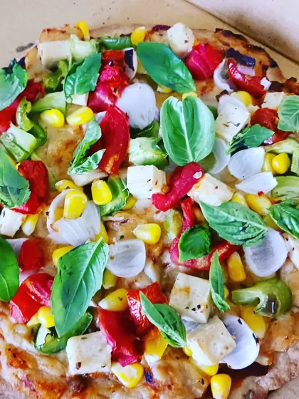 A vibrant pizza on a millet base, topped with fresh basil, corn, bell peppers, and a special cheese made from millet milk. This is a fantastic collaboration of healthy ingredients.