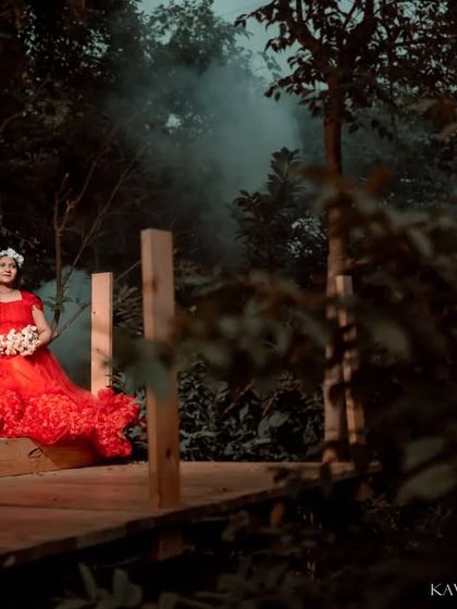 A dramatic and elegant solo maternity portrait. The flowing red gown against the moody, wooded backdrop with a touch of theatrical smoke creates a powerful, fairytale-like image of motherhood.