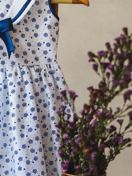 A lovely white cotton dress with a blue floral block print. The navy blue sailor collar and bow add a classic, nautical-inspired touch.