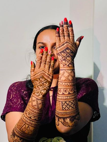 A beautiful bride showing off her full-arm mehendi, which includes personalized initials and elephant motifs.