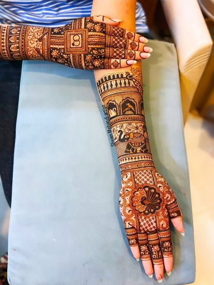 A stylish layout of a full-arm mehandi, featuring a peacock on the palm and wedding ring motifs.