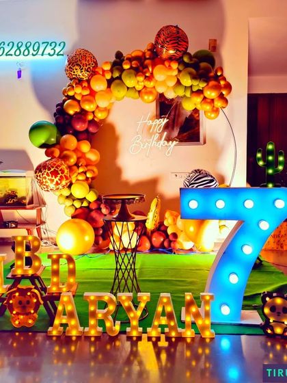 A surprise jungle theme birthday for Aryan, featuring a neon sign, marquee letters, and artificial palm trees to create a tropical vibe at night.