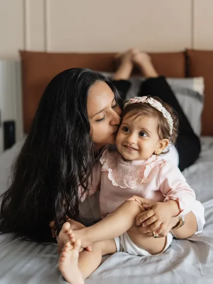 A tender kiss for her baby girl. This lifestyle photo, taken in a relaxed home setting, captures the sweet, everyday moments of motherhood.