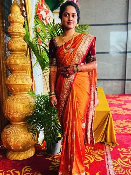 A full-length view of a client ready for her pre-wedding function. The look features natural-looking makeup and a simple, elegant hairstyle that works beautifully with her orange silk saree.