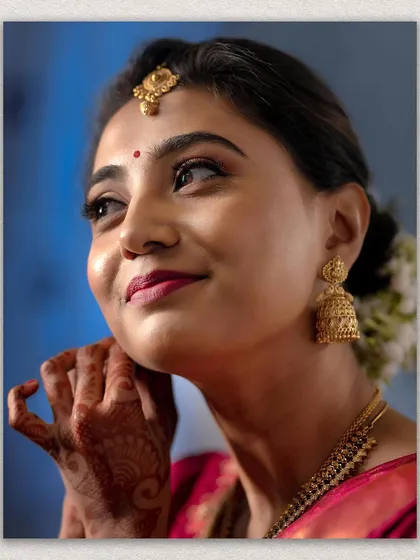 A radiant close-up of a bride, capturing her joyful expression and beautiful makeup. The focus on her traditional jhumkas and henna-adorned hand adds to the bridal charm.