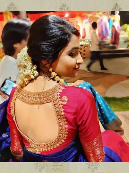 The back of this red and blue saree blouse features a large, elegant cutout framed by intricate gold embroidery. This design element adds a touch of modern sophistication to a traditional outfit.