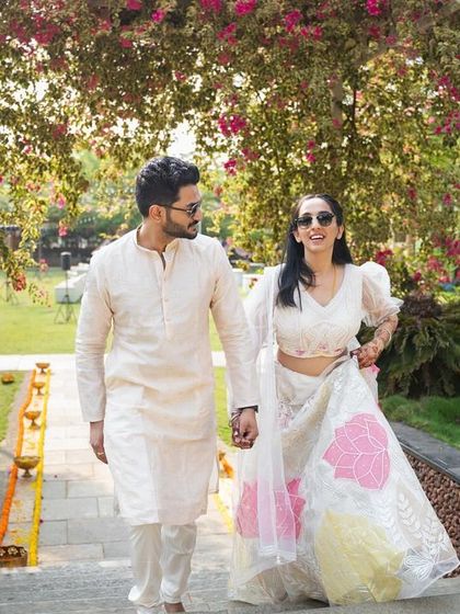 A candid moment from a Haldi ceremony, where the couple shares a playful and affectionate look against a backdrop of white flowers and greenery.