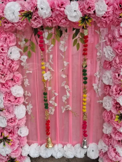 This is a classic floral frame design for a small pooja space. The backdrop is made with pink and white artificial carnations and includes hanging beaded strings with bells for a traditional touch.