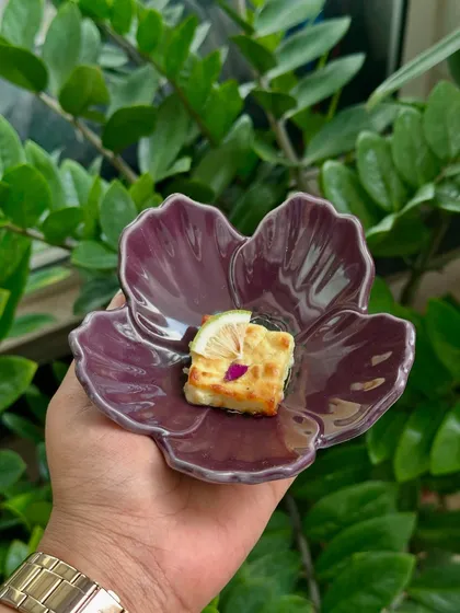 A bite of Gondhoraj Paneer Tikka, a dish from our traditional Bengali menu, served in a beautiful purple flower-shaped bowl.