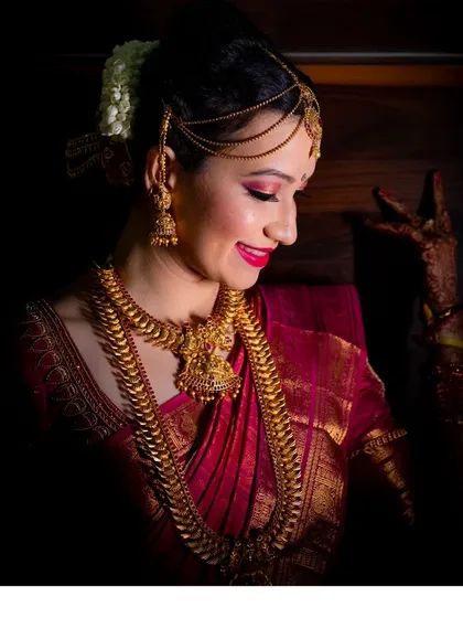 A beautiful, classic bridal portrait. The focus is on the bride's serene expression and her stunning traditional jewelry and red saree.