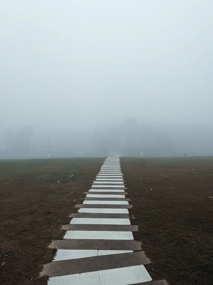 A striped pathway disappears into the dense fog. This minimalist and symmetrical composition creates a sense of journeying into the unknown, highlighting the abstract beauty of a foggy day.