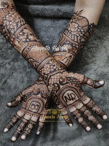 For your engagement, we can create a design that is both traditional and personal. This intricate mehendi features the couple's initials, 'ND', and interlocking rings, surrounded by classic peacock and floral motifs that extend up the forearm.