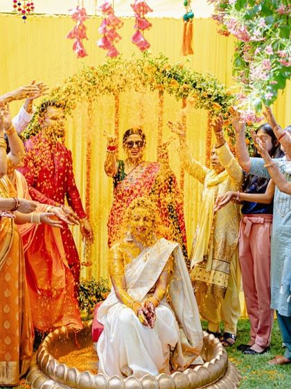 A bride being showered with marigold petals during her Haldi ceremony, a vibrant and joyous moment surrounded by loved ones.
