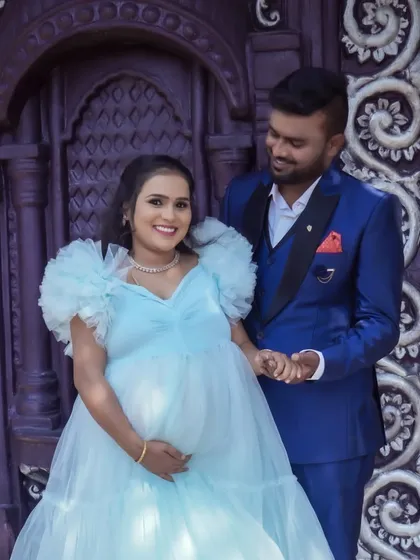 A stylish couple poses in front of an ornate door. The contrast between his sharp suit and her soft, flowing gown makes for a visually interesting and fashionable maternity photo.