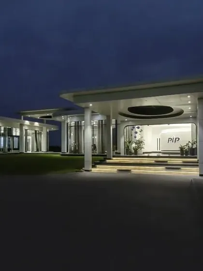 The same institutional building viewed at dusk, with interior lighting creating a warm glow. This highlights the building's transparency and showcases its structure against the evening sky.