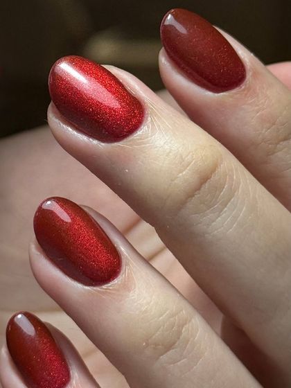 A deep, metallic red polish with a subtle shimmer. This color has incredible depth and looks luxurious on these well-manicured oval nails.