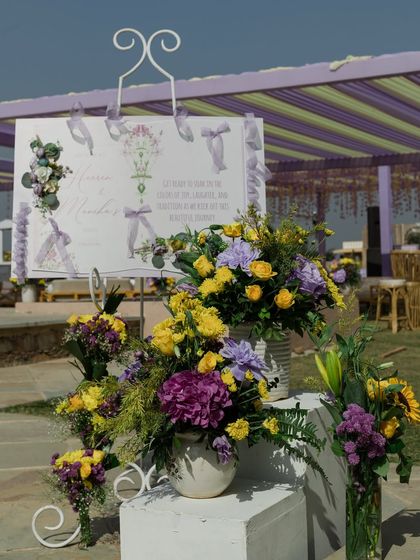 A welcome sign for the Haldi, surrounded by lush arrangements of yellow and purple flowers, tying into the event's color scheme.