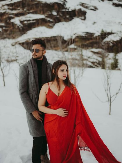 A stylish and moody shot of a couple in the snow, the bride's red saree adding a pop of color.