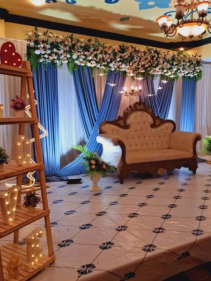 A beautiful stage setup with blue and white drapes, a floral header, and an elegant sofa. The "LOVE" marquee letters on the side add a romantic touch.